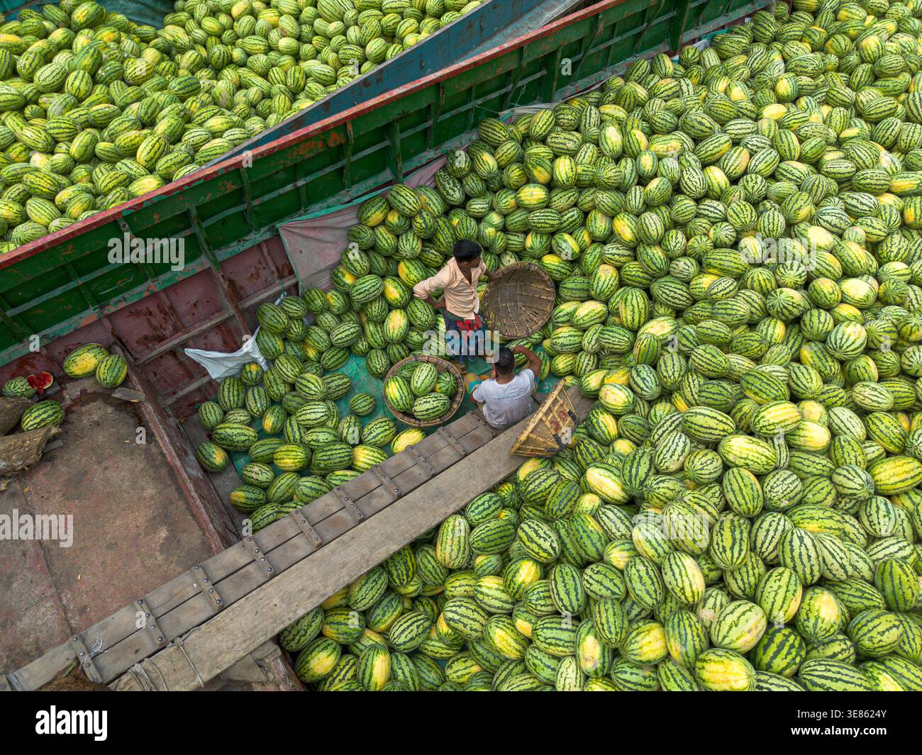 Dacca, Bangladesh - 4 aprile 2026: Vista aerea di un vivace mercato fluviale traboccante di innumerevoli meloni a strisce verdi e gialle, dove lavorano i venditori Foto Stock