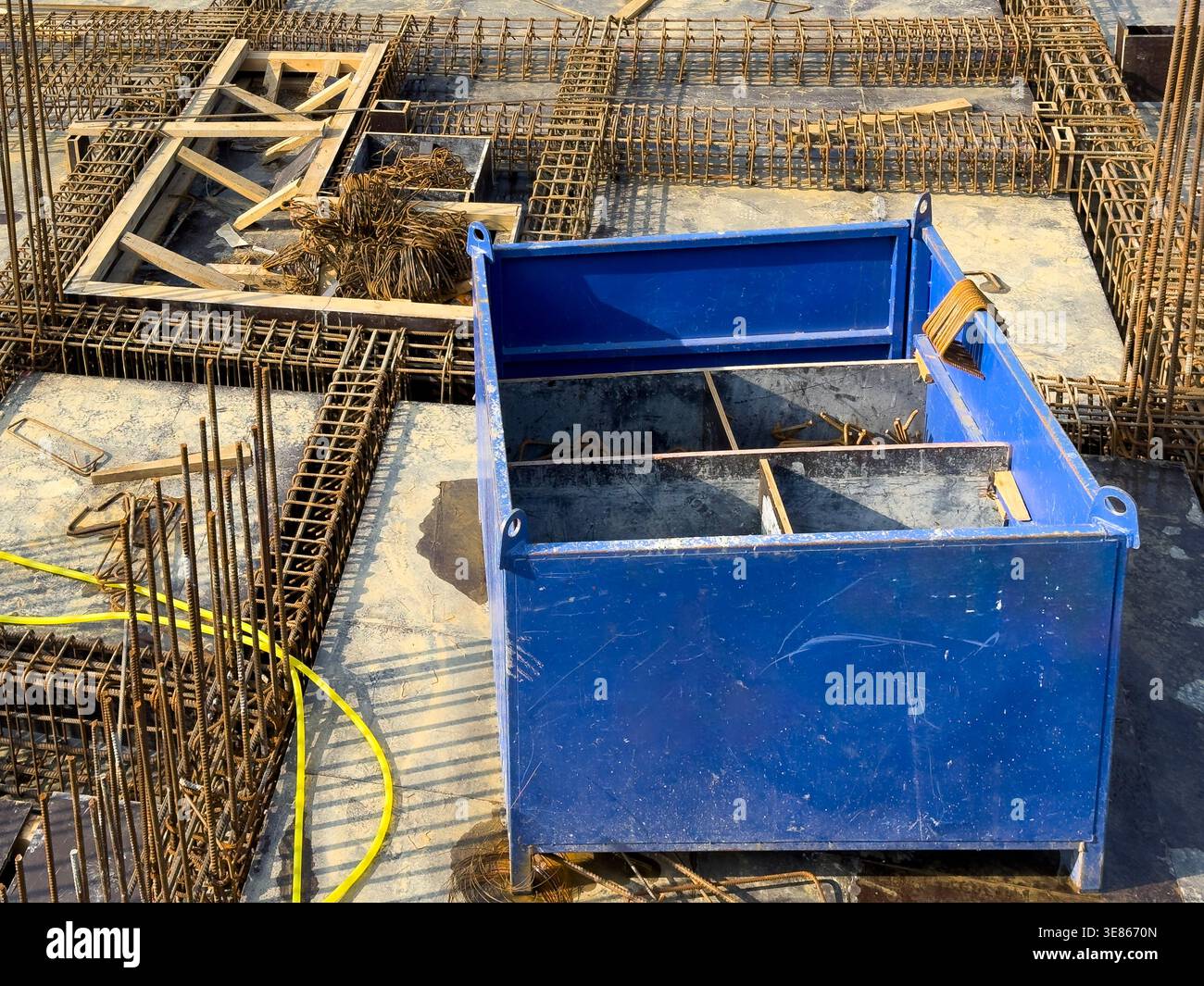 Primo piano di una fondazione in calcestruzzo in costruzione con gabbie per tondini in acciaio, casseforme e una cassetta di stoccaggio in metallo blu in loco, che mostra edifici e civili Foto Stock