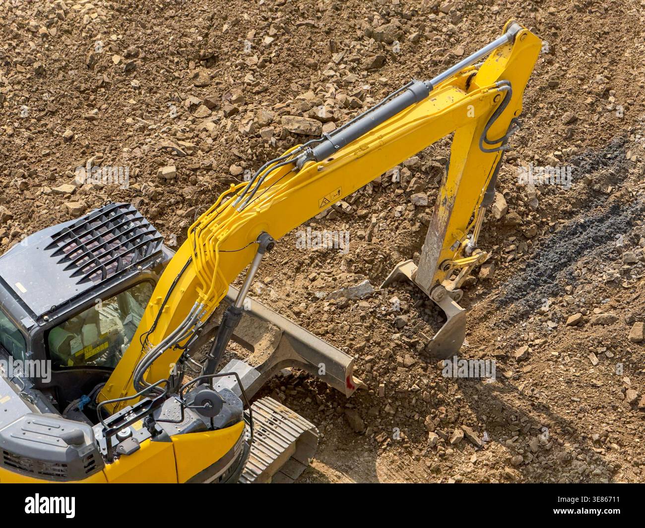 Vista dall'alto ad angolo elevato di un escavatore idraulico giallo che lavora in cantiere, scavo e spostamento di terreno e ghiaia in un'area di lavorazione del terreno con sgrossatura Foto Stock