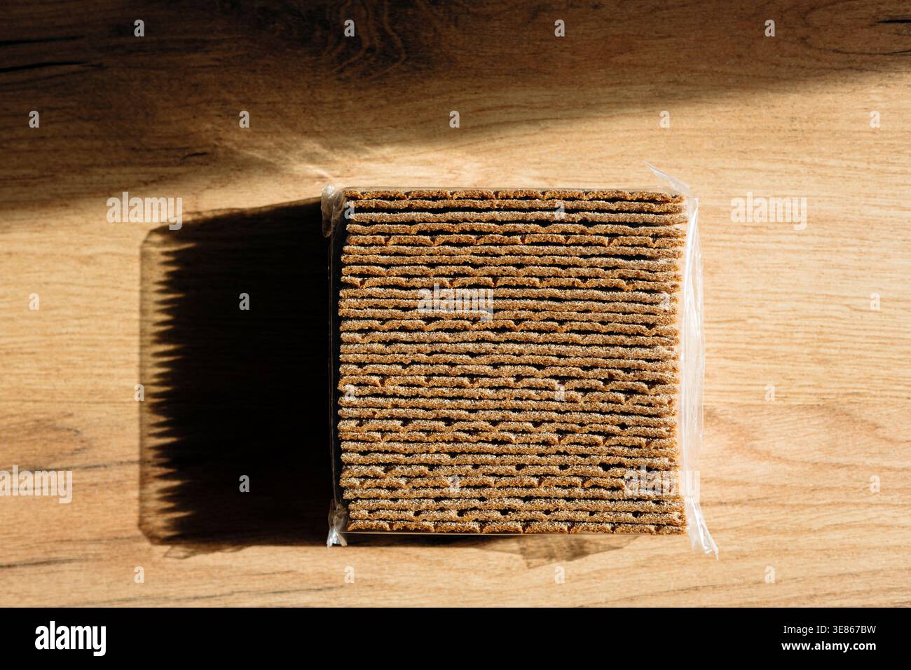Una pila dettagliata di pane croccante di segale si trova su una superficie di legno, che proietta una lunga ombra in un'illuminazione soffusa. Perfetto per spuntini attenti alla salute o per un me leggero Foto Stock