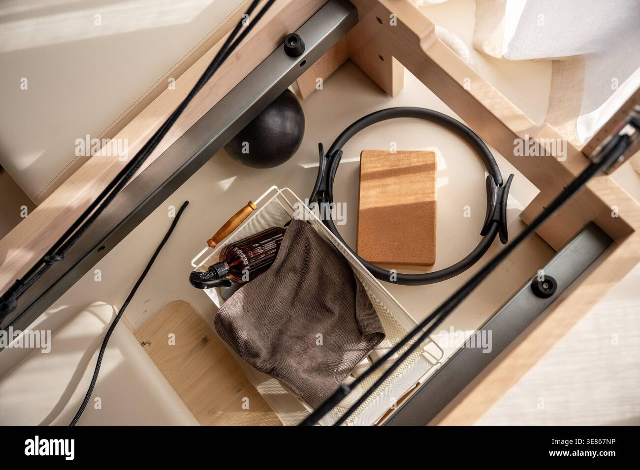 Vista dall'alto degli accessori Pilates Reformer, tra cui anello, blocco di sughero, palla e asciugamano in un luminoso studio minimalista, pronto per l'allenamento benessere. Foto Stock
