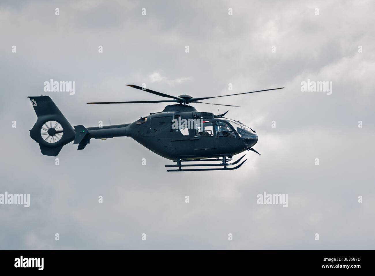 Vista laterale di un elicottero moderno in volo contro un cielo nuvoloso coperto, che mostra le pale del rotore e la ventola della coda. Sfondo minimo con ampio spazio di copia Foto Stock