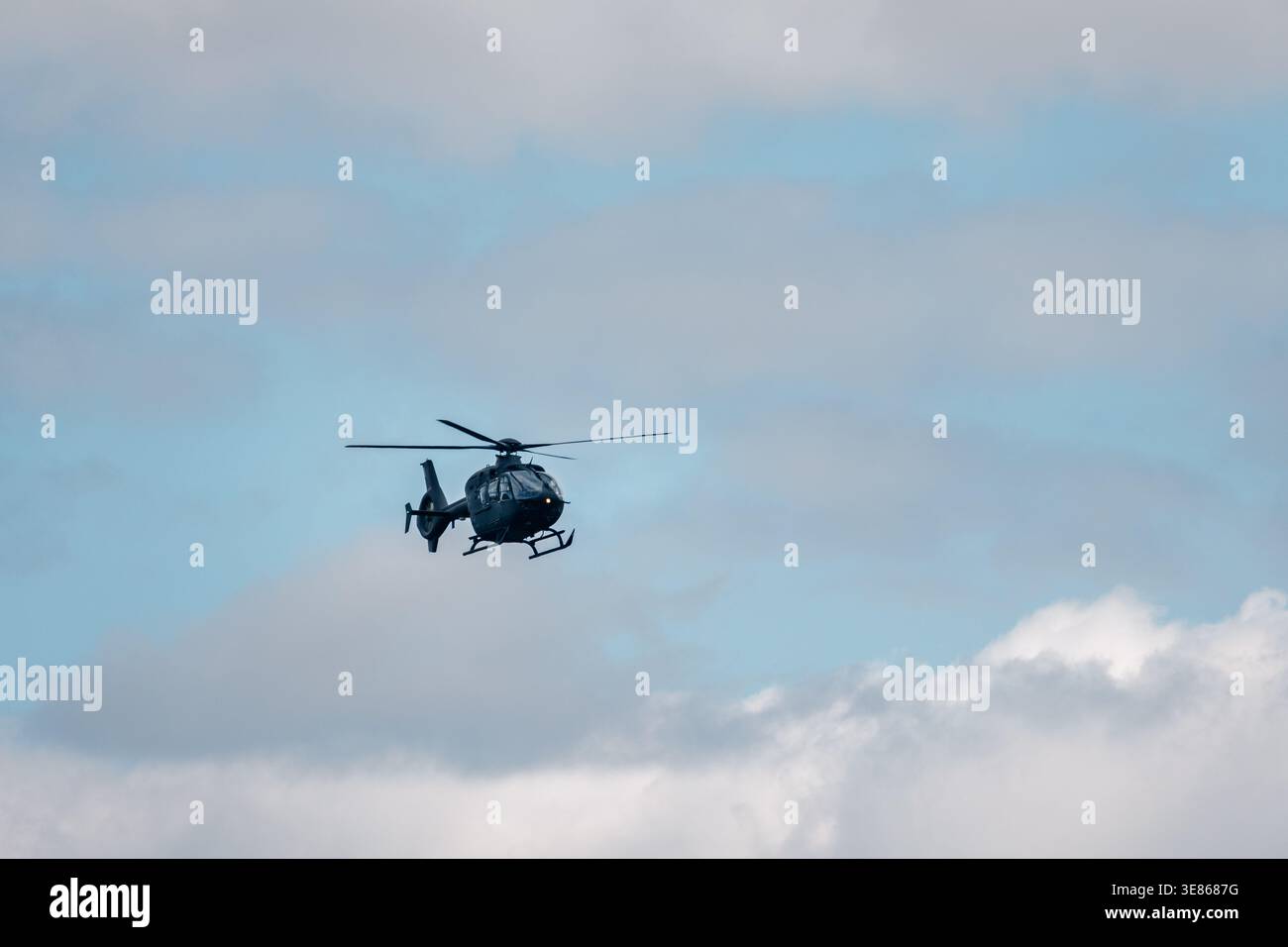 Un singolo elicottero vola in alto contro un cielo blu nuvoloso, catturato da lontano con ampio spazio di copia, trasportando viaggi, pattuglia, salvataggio e aviazione Foto Stock