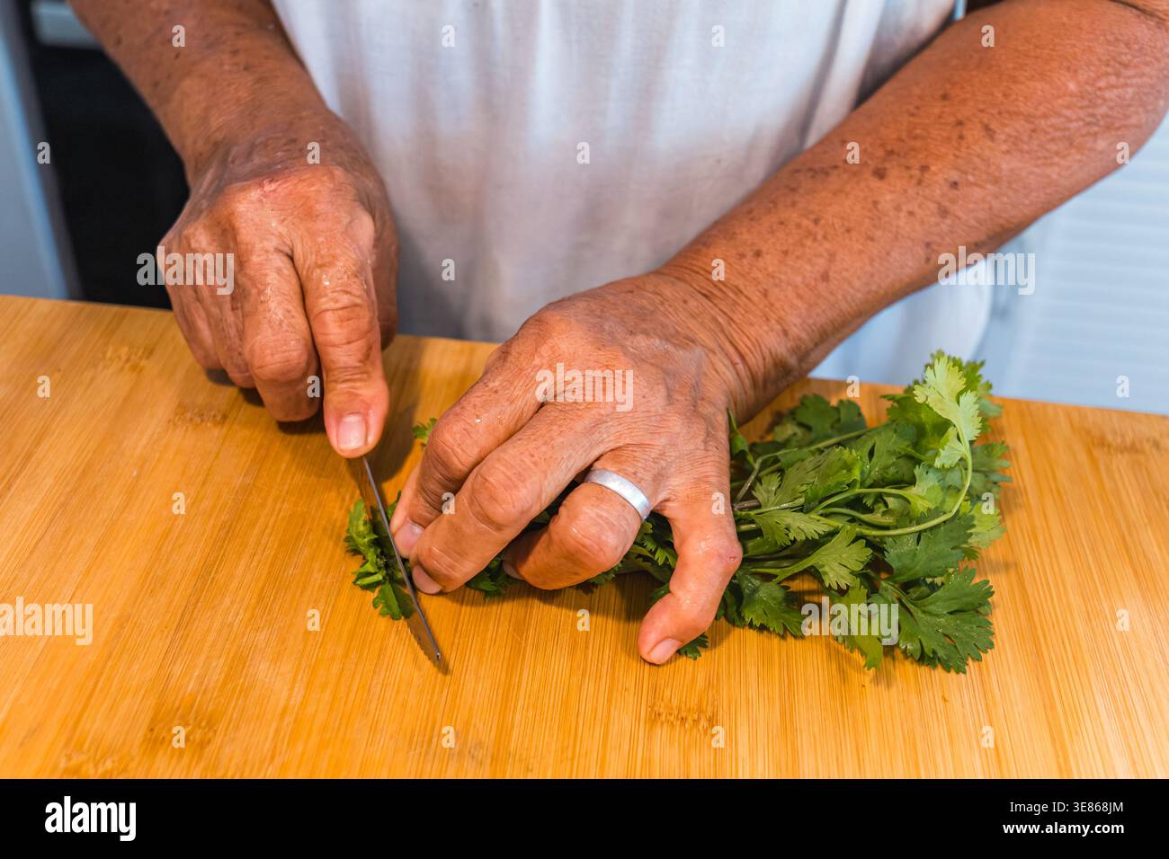 Un paio di mani trita sapientemente coriandolo fresco su un tagliere di legno. Questo primo piano cattura l'essenza della cucina caraibica con erbe tropicali Foto Stock