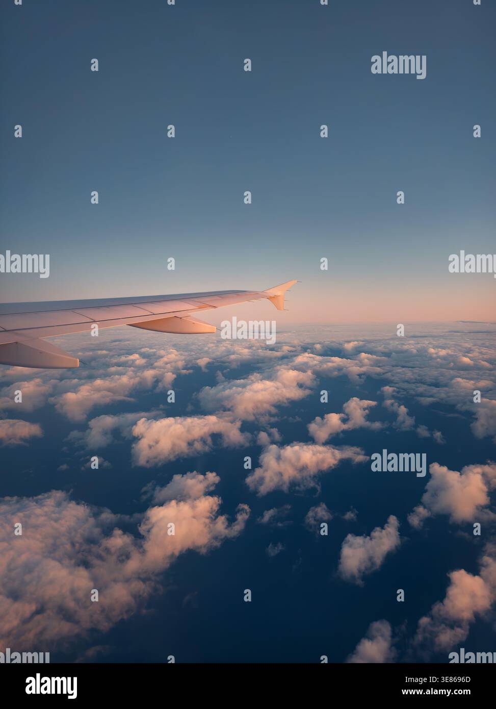 Vista dell'ala dell'aeroplano sopra le soffici nuvole invernali sul mare, con sfumature del tramonto nel cielo. Catturato da un volo in avvicinamento a Tenerife, evidenziando la vittoria Foto Stock