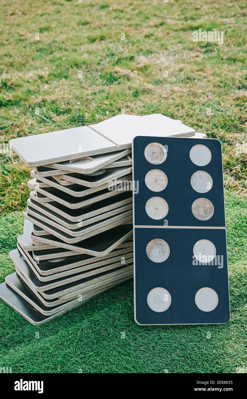 Primo piano di tessere di domino impilate sull'erba con una tessera in piedi davanti. Composizione pulita per esterni che simboleggia strategia, preparazione, pianificazione e. Foto Stock