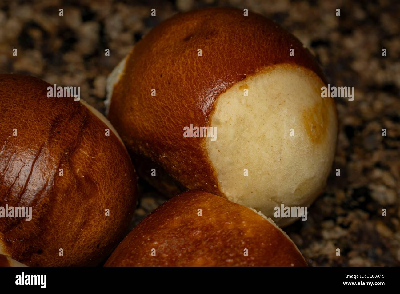 Foto macro di rotoli di pretzel marrone dorato con una crosta lucida e morbide texture interne su una superficie di granito scuro Foto Stock