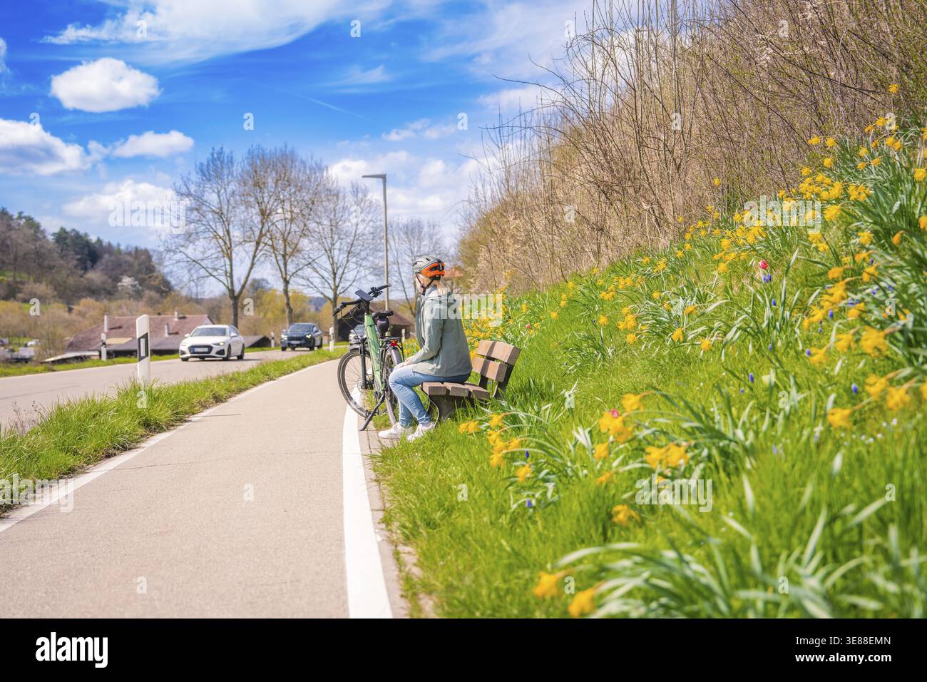 Persona in bicicletta su una panchina illuminata dal sole circondata da flora fiorente, tour in bicicletta elettrica, Aidlingen, regione di Hecken e Gaeu, distretto di Boeblingen, Germania Foto Stock