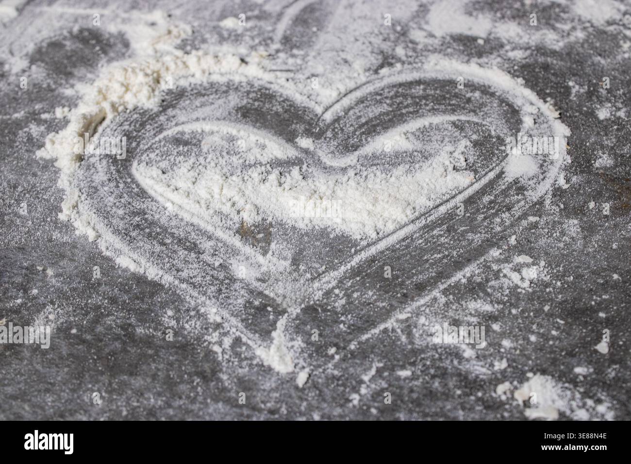Un'impressione a forma di cuore nella farina su una superficie rustica, che simboleggia l'amore e la creatività culinaria Foto Stock