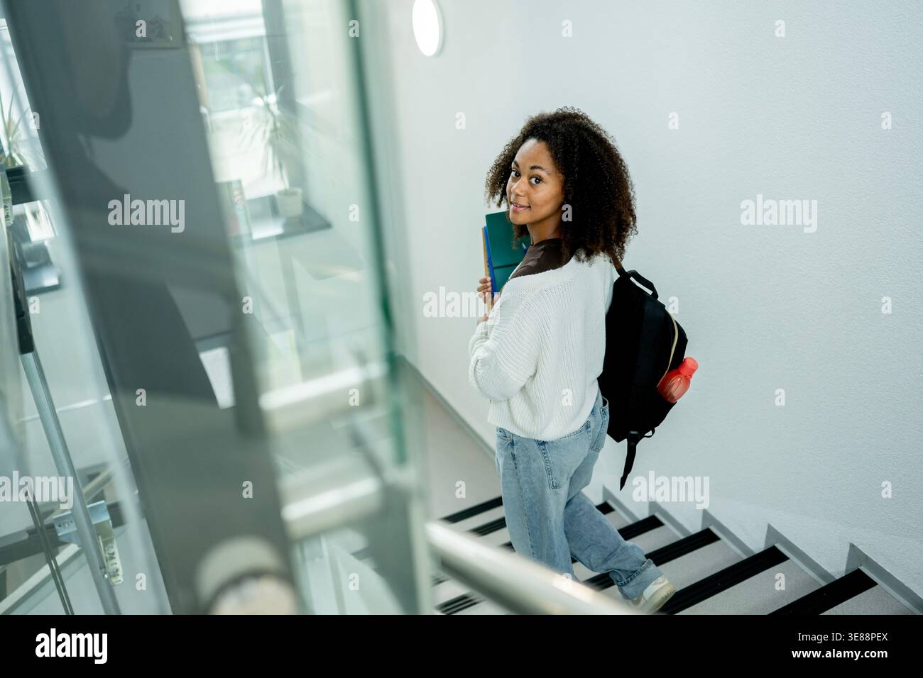 Studente universitario che si sposta attraverso l'edificio con materiali di studio e zaino. Foto Stock