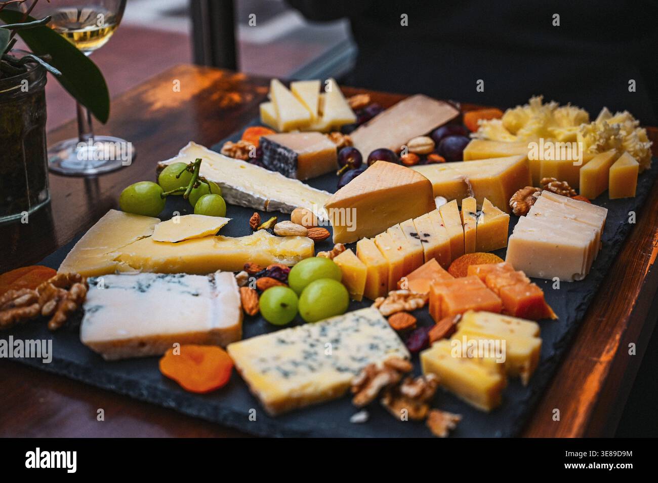 Tagliere di formaggi assortiti con uva, noci e frutta secca serviti su un piatto di ardesia in un ristorante. Foto Stock