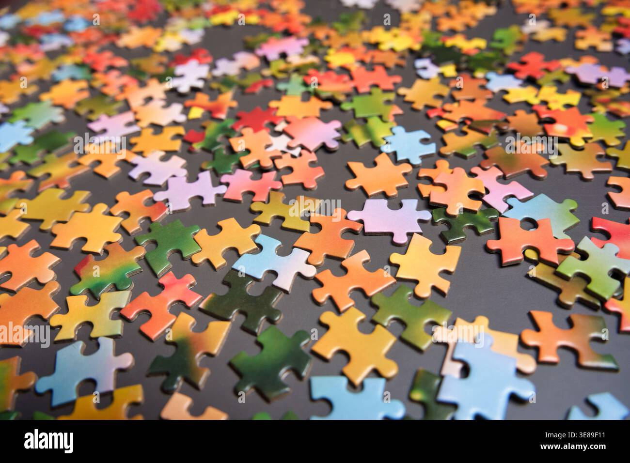 Visuale grandangolare di numerosi pezzi di puzzle multicolore distribuiti su una superficie di colore grigio scuro. Messa a fuoco selettiva sugli elementi in primo piano. Perfetto per conc Foto Stock