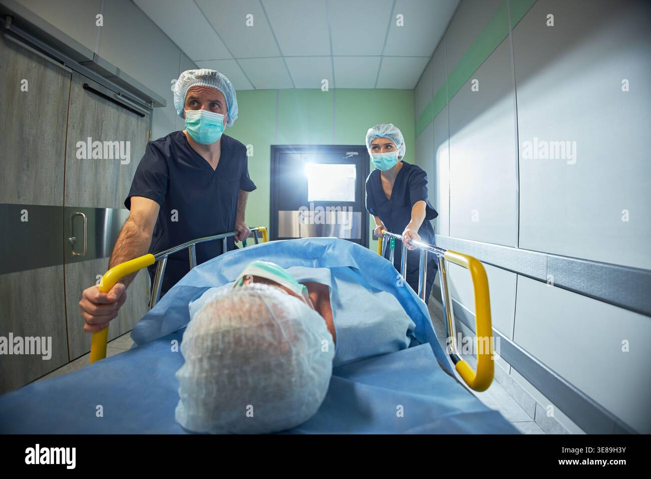 Ampio angolo di visione dei chirurghi di mezza età che corrono il paziente sulla barella attraverso il corridoio dell'ospedale per operazioni urgenti. Adatto per l'emergenza sanitaria, la chirurgia, il triage, la cura ospedaliera marketing Foto Stock