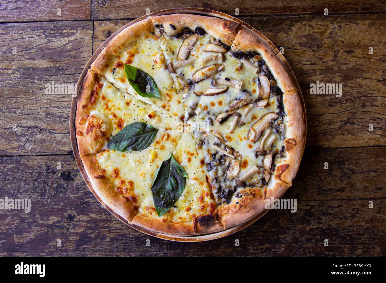 La pizza appena sfornata su un tavolo di legno è condita generosamente Foto Stock