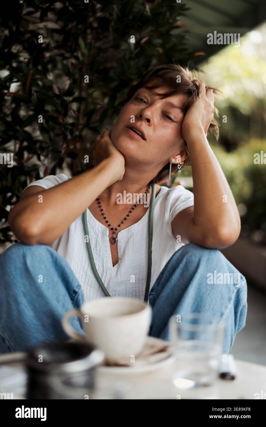 Donna che vive un momento burnout seduto da sola all'aperto con un caffè Foto Stock