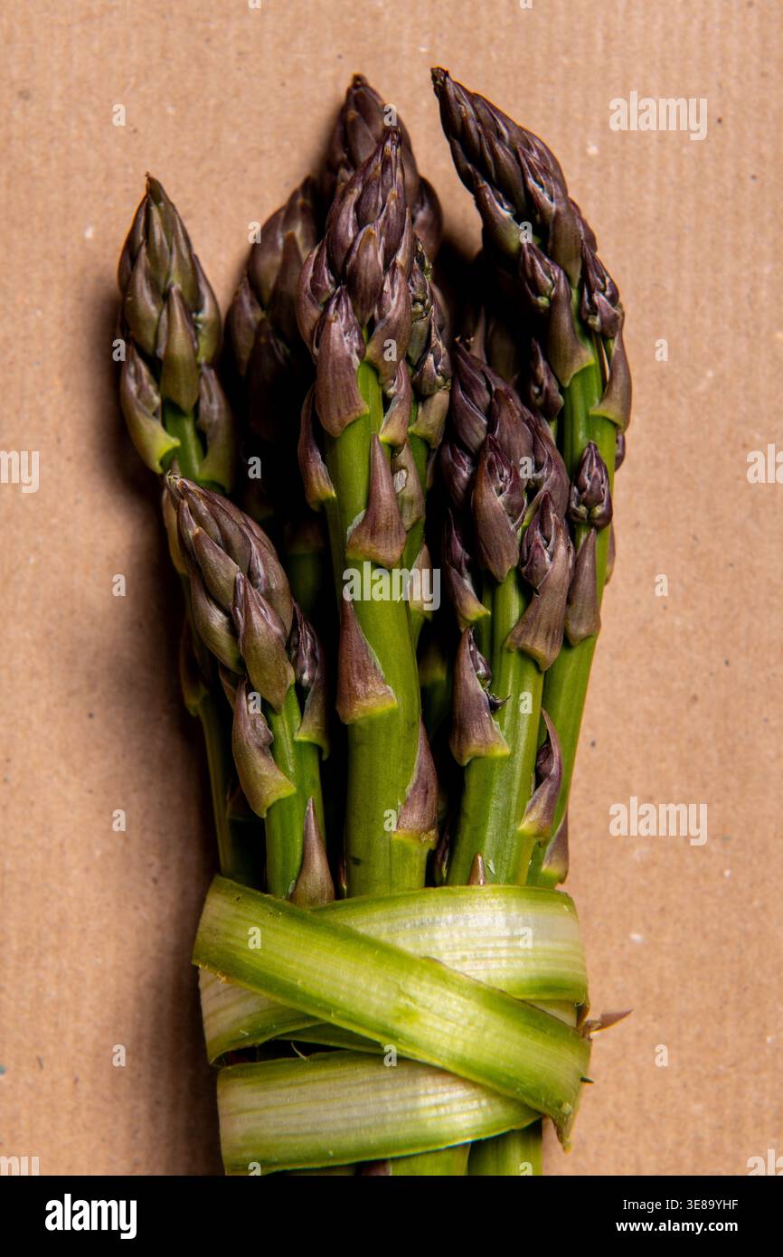 Asparagi freschi legati con il nastro su marrone. Foto Stock