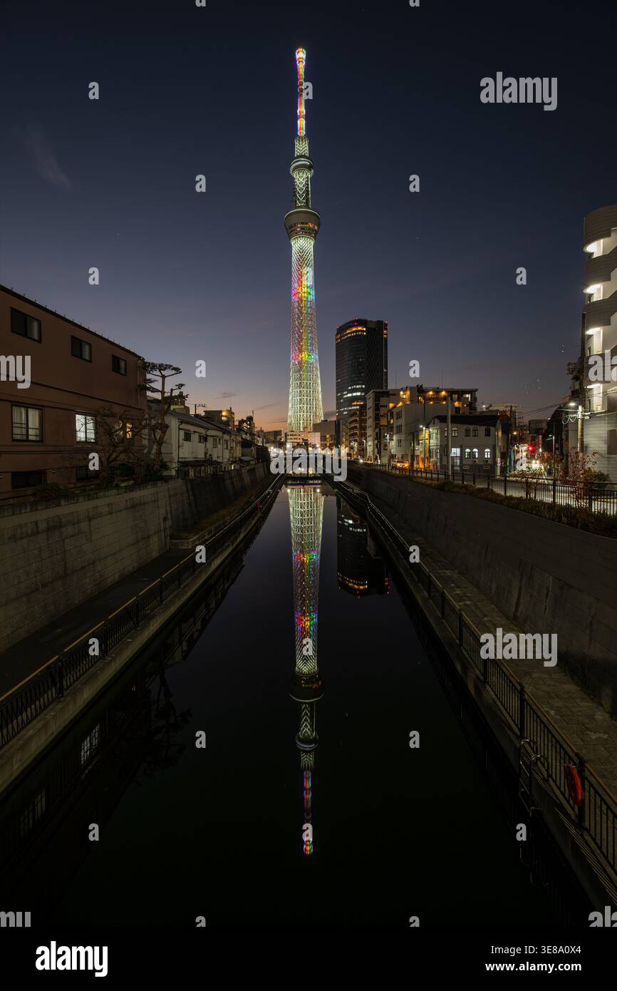 Vista notturna dello Skytree di Tokyo e del suo perfetto riflesso sul fiume Kitajukken dal Ponte Jukken, caratterizzato da una rara illuminazione arcobaleno Foto Stock