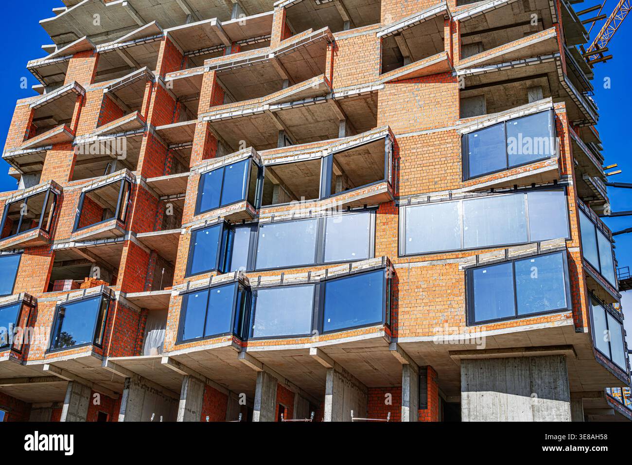 Un moderno edificio residenziale in costruzione caratterizzato da mattoni arancioni e finestre in vetro. Foto Stock