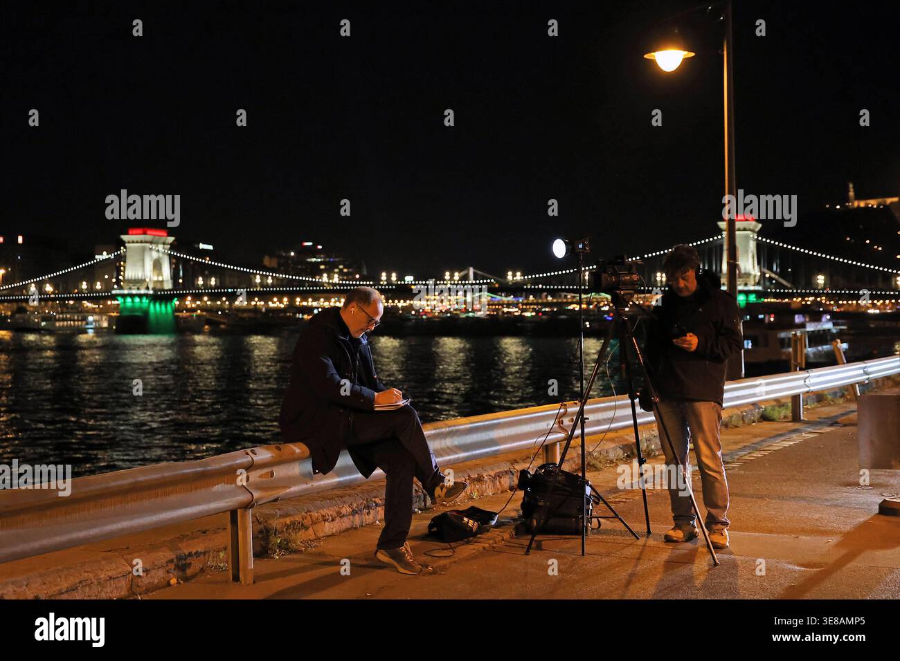 Giornalisti sulla riva del Danubio a Budapest con la Chain ​Bridge illuminata nei colori nazionali ungheresi la notte delle elezioni del 2026 Foto Stock