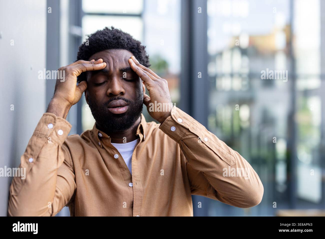 Giovane che soffre di forte mal di testa e emicrania, che preme le mani verso i templi, si sente esausto e sopraffatto dalla pressione mentale, soffre di stress e bruciature mentre si trova all'aperto Foto Stock