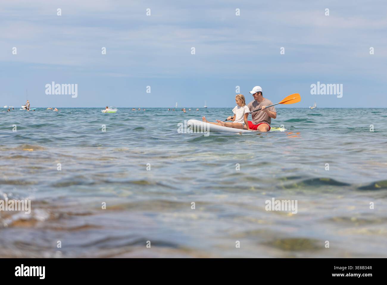 Il padre e la figlia pagaiano insieme su una tavola in piedi durante una giornata estiva al mare. Condividono tempo di qualità e divertimento. Foto Stock