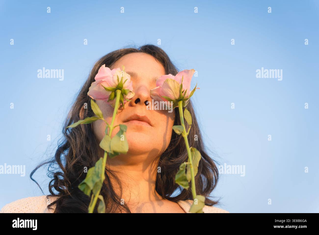 giovane donna millenaria con fiori davanti agli occhi contro il cielo blu, con rose in mano, ha umore primaverile, gode di un odore piacevole in primavera Foto Stock
