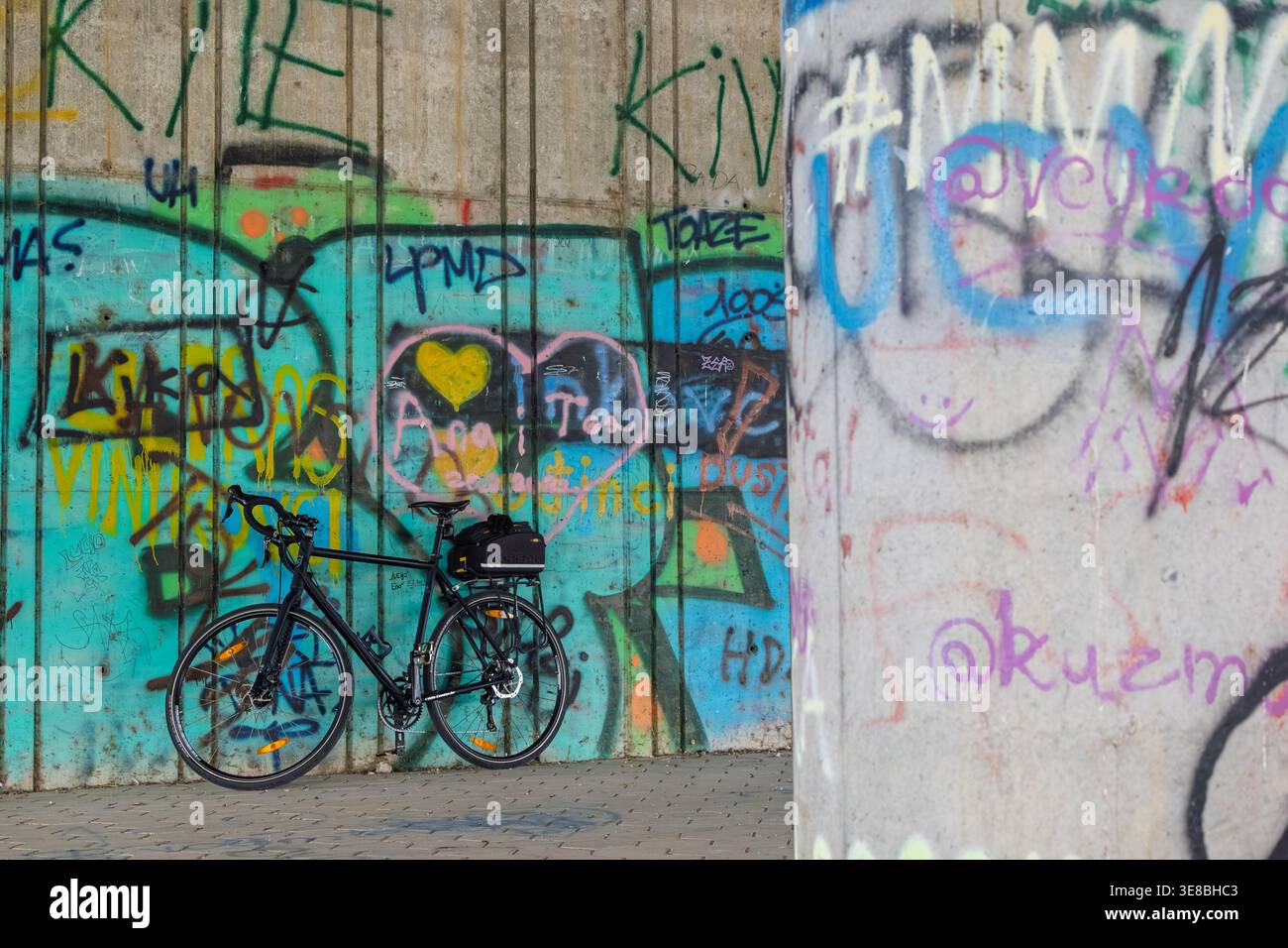 Una bicicletta solitaria si appoggia su una vibrante parete di cemento rivestita di graffiti in un sottopassaggio urbano, trasmettendo energia per la Street art, contrasto di colore e senso Foto Stock
