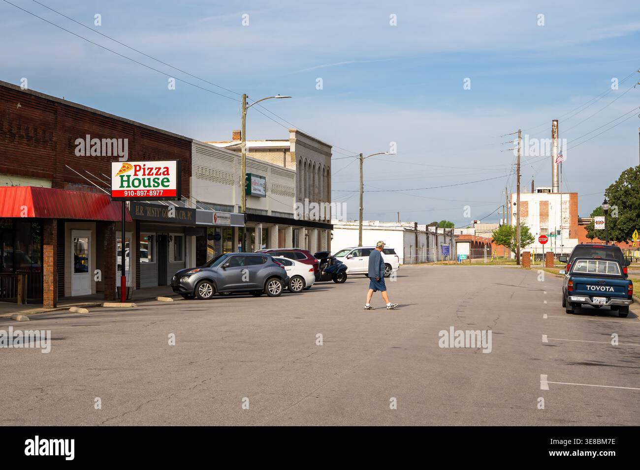 Un'area pedonale attraversa una strada del centro di Erwin, North Carolina, con strutture storiche di un impianto tessile sullo sfondo. Foto Stock