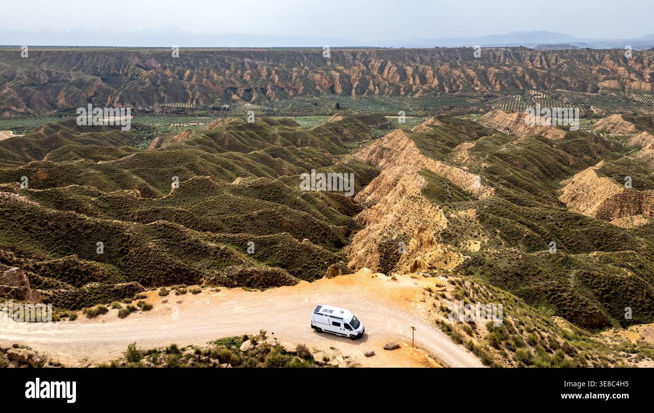 Un camper bianco viaggia lungo una solitaria strada sterrata su un crinale nel Granada Geopark. Quest'ampia vista aerea rivela gli infiniti calanchi e le Foto Stock