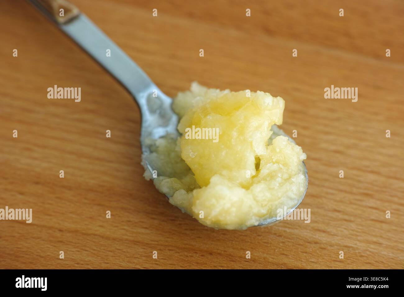 Un cucchiaio da tè con una porzione di olio di cocco giallo. Sfondo in legno. Primo piano. Foto Stock