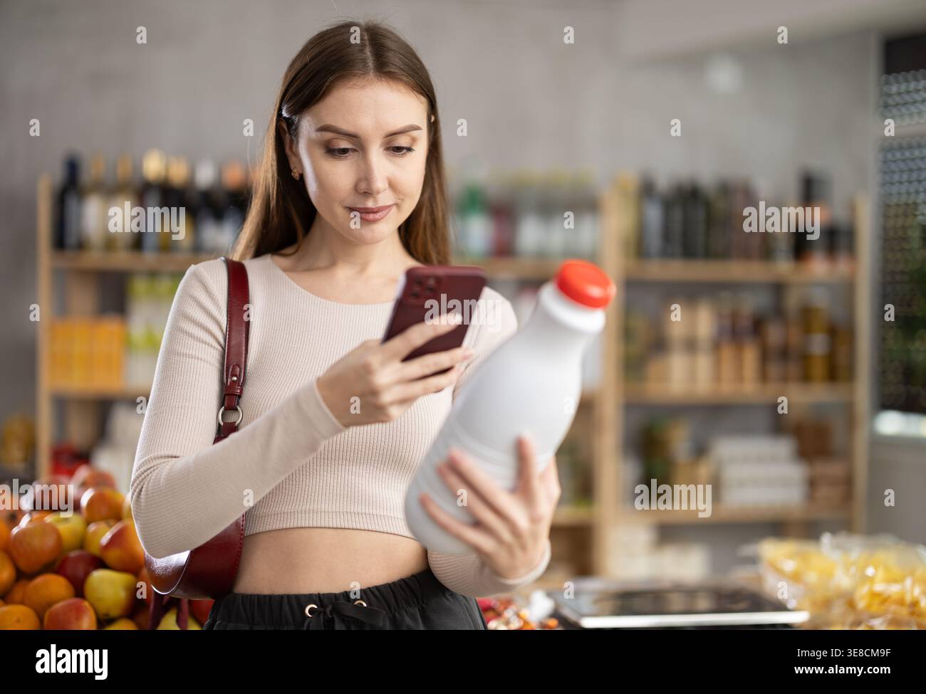 L'acquirente donna verifica l'idoneità - scansiona il codice QR sull'etichetta del flacone di latte nel negozio di alimentari Foto Stock