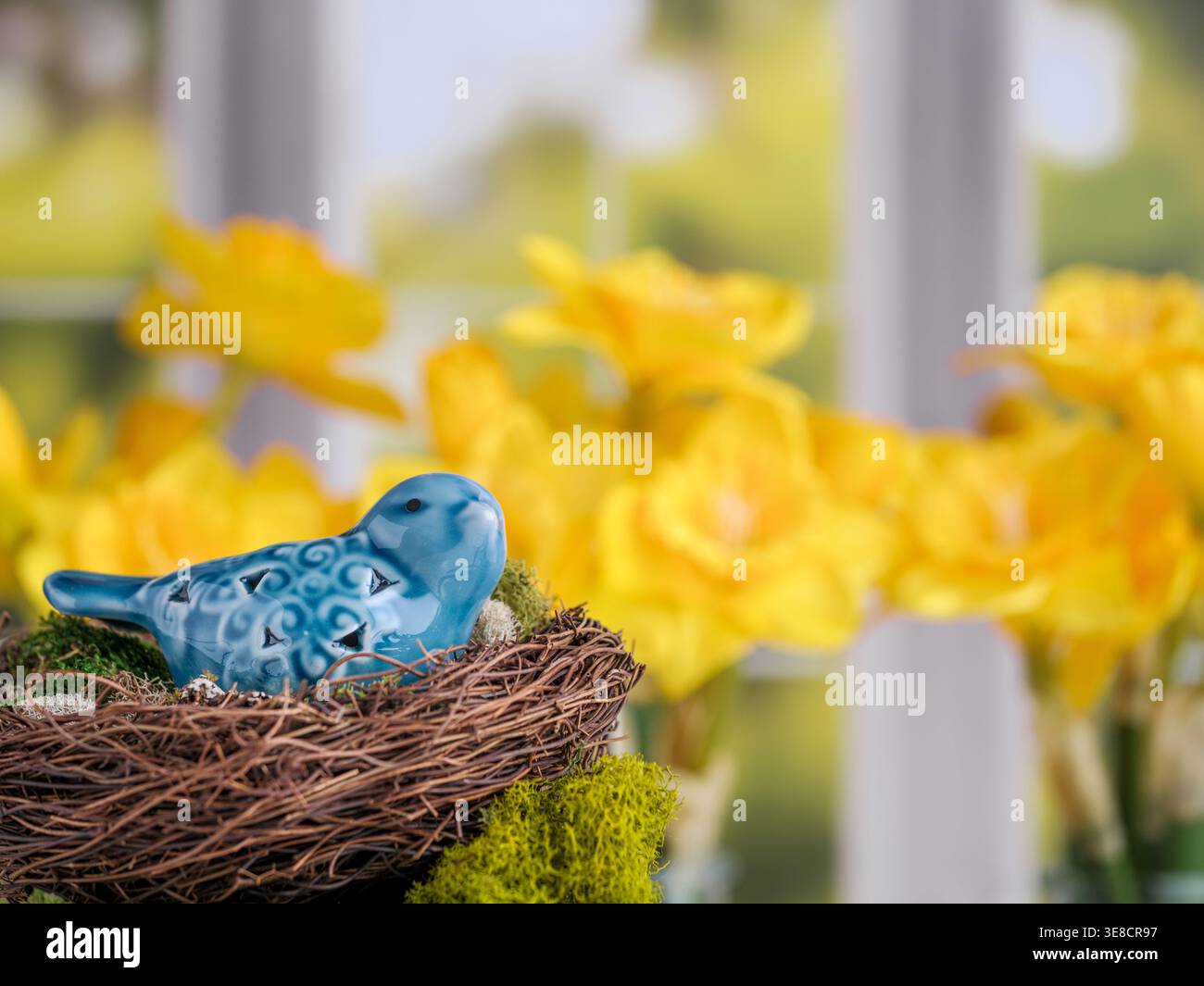 Figurina di uccello in ceramica blu nel nido con fiori di narcisi colorati e allegri di primavera e sfondo sfocato della finestra del giardino Foto Stock