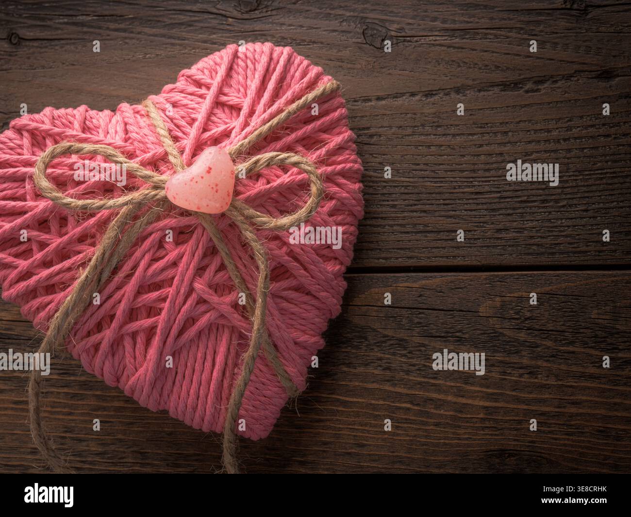 Cuore rustico in filato rosa San Valentino con fiocco in spago di iuta e fondo in legno. Sfondo personalizzato per San Valentino Foto Stock