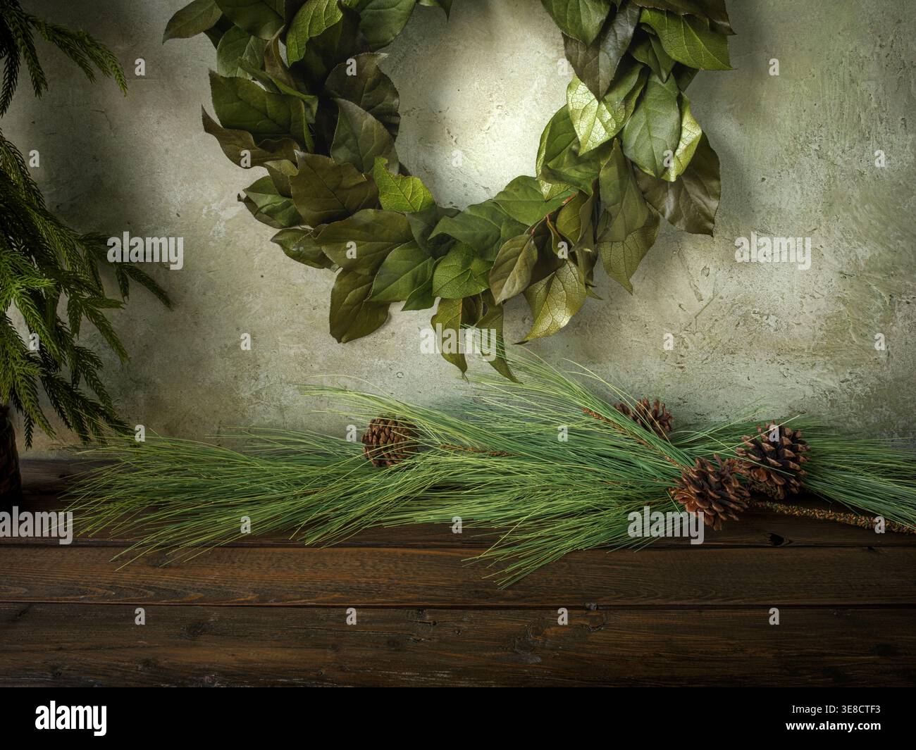 Sfondo per il biglietto di Natale personalizzato. Corona appesa su fondo in gesso rustico e tavola in legno. Pino Norfolk e aghi lunghi, pinne Foto Stock