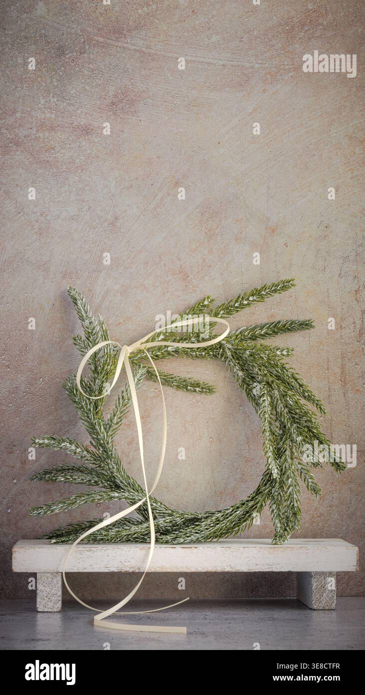 Sfondo per il biglietto di Natale personalizzato. Corona di pino Norfolk boho chic verticale, arco a nastro bianco su legno intemprato, supporto bianco su sfondo rustico Foto Stock