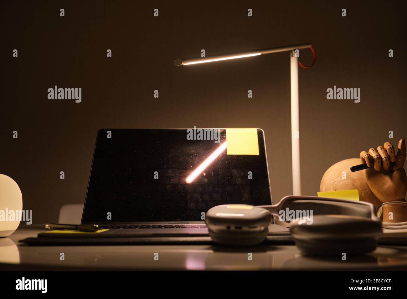 Spazio di lavoro con laptop, cuffie, lampada moderna e vari materiali di studio durante la notte Foto Stock