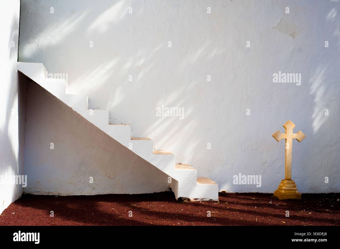 Ironia della vita e della morte: Scala bianca minimalista verso il nulla e croce di pietra presso l'Antico Cimitero di Teguise, Lanzarote. Foto Stock