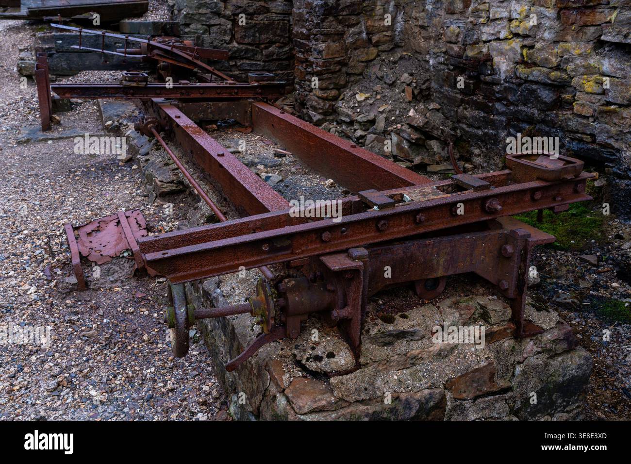Vista ravvicinata dei macchinari in ferro arrugginito e delle guide metalliche posizionate contro le pareti in pietra del vecchio mulino abbandonato Foto Stock