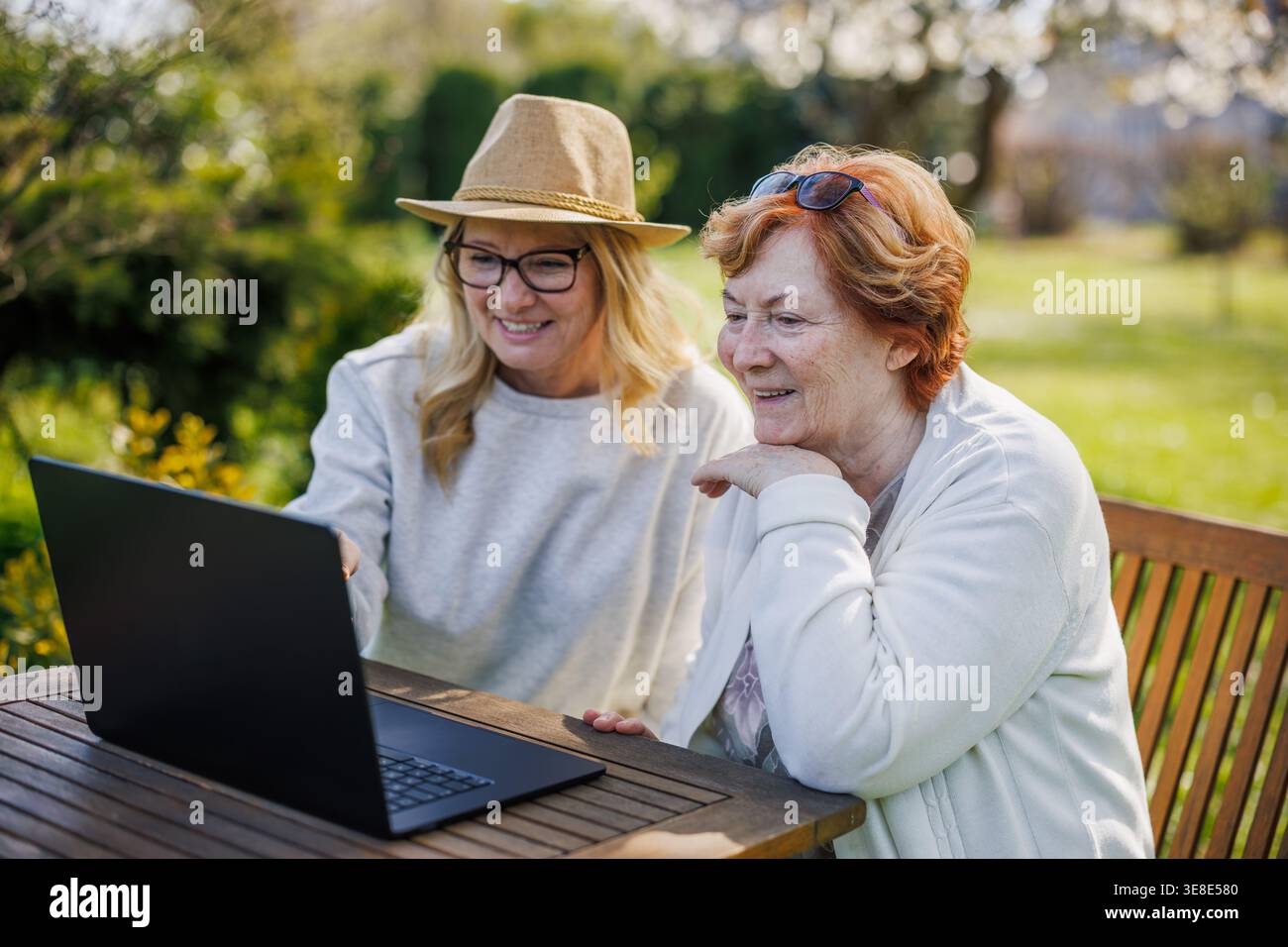 Famiglia multigenerazione che utilizza la tecnologia. Figlia adulta che insegna alla madre anziana come effettuare videochiamate sul laptop mentre si siede al tavolo all'aperto Foto Stock