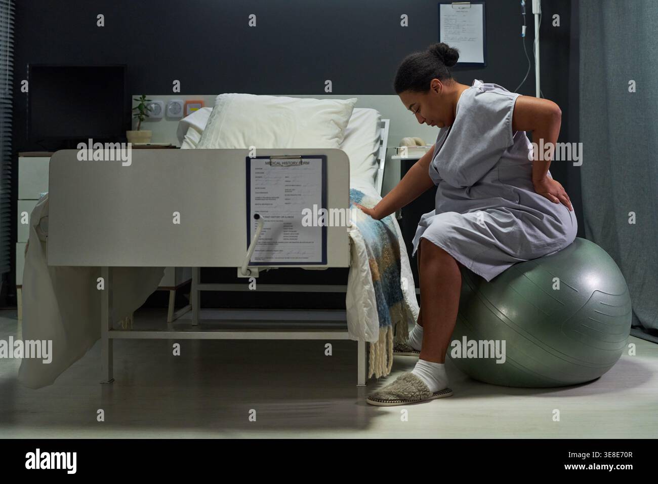 Colpo largo di donna incinta seduta su palla di esercizio accanto al letto d'ospedale, gestire il dolore al travaglio. Sostenere l'assistenza alla maternità, l'educazione al parto, il marketing in clinica prenatale Foto Stock