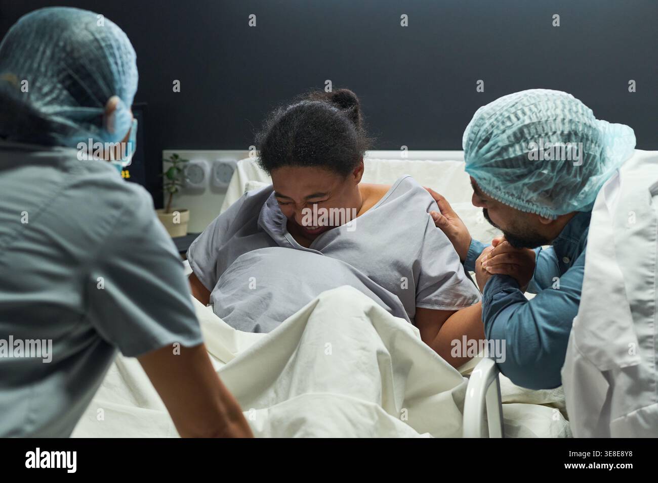 Donna che partorisce nel letto d'ospedale, sostenuta dal partner e dall'infermiere durante il travaglio. Concetto di assistenza sanitaria di squadra e maternità per ostetricia, genitorialità, marketing assicurativo Foto Stock