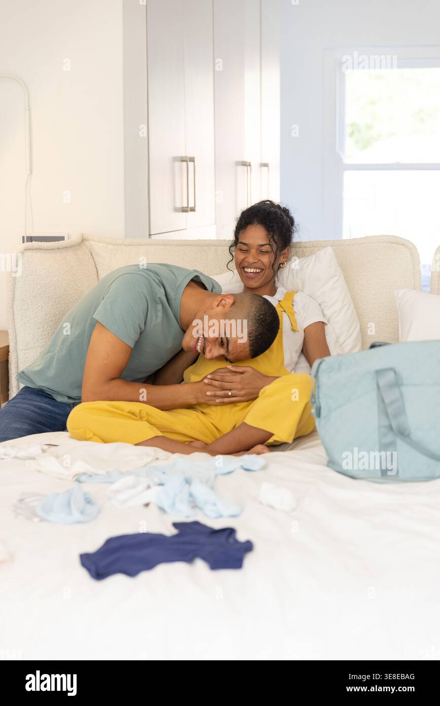 Coppia afroamericana seduta sul letto in una camera da letto con una tuta che tiene la testa in mezzo a una borsa per pannolini Foto Stock