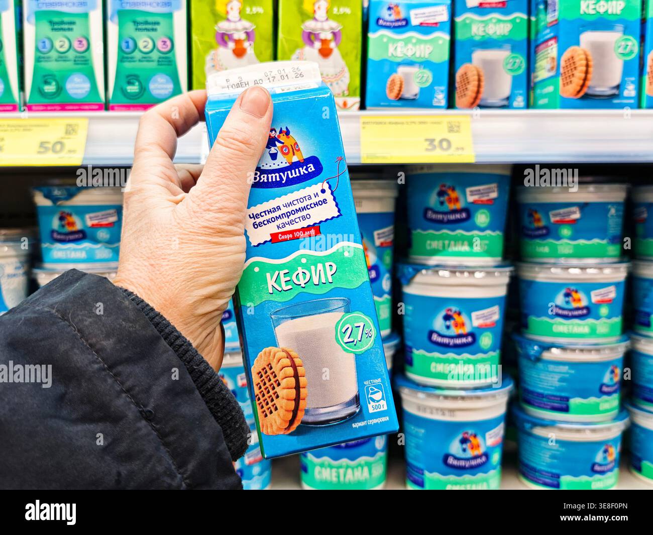 Kirov, Russia - 12 gennaio 2026: Un acquirente seleziona un cartone in un corridoio di un negozio di alimentari circondato da scaffali pieni di prodotti caseari e spuntini durante Foto Stock
