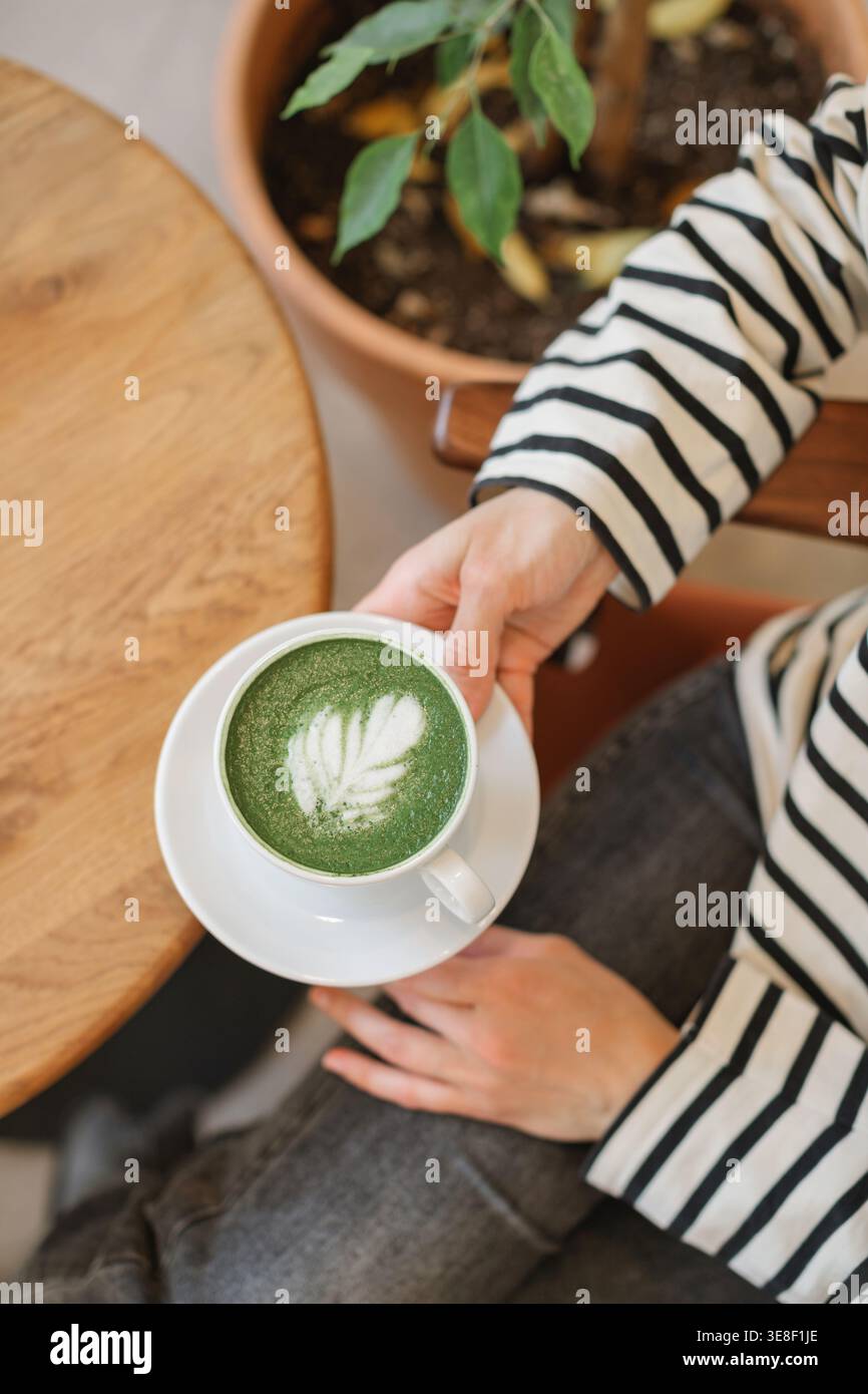 Vista dall'alto di una donna seduta in un cafÃ© che beve un latte matcha caldo Foto Stock