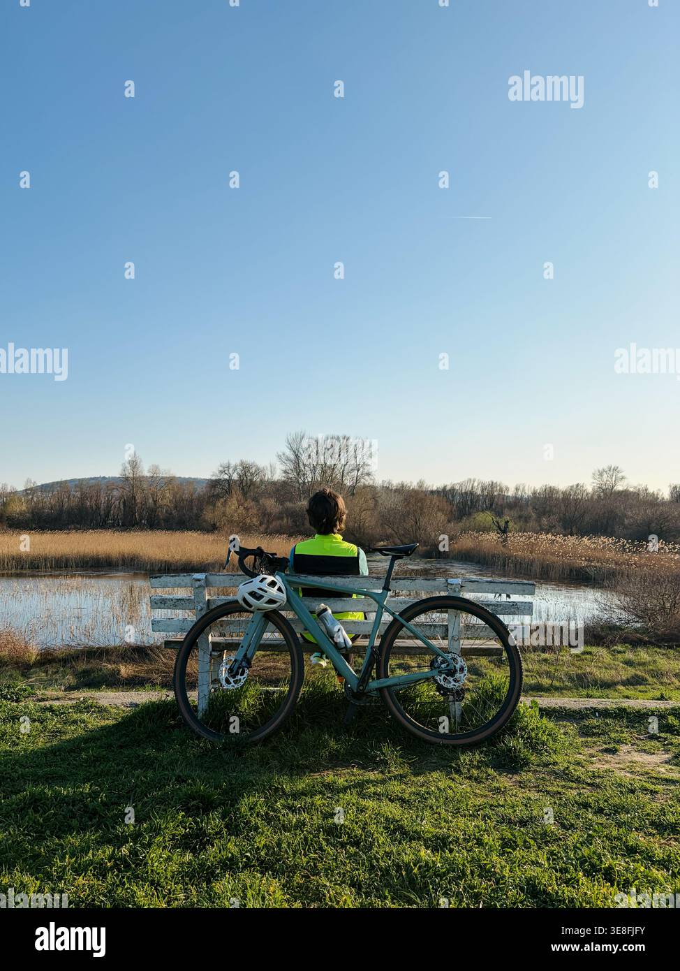 Ciclista seduto su una panchina con bicicletta gravel vicino a un lago tranquillo nella natura. Concetto di riposo, viaggio e stile di vita attivo all'aperto. Foto Stock