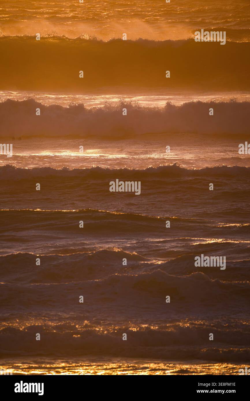 Vista aerea delle onde ondulate dell'oceano con schiuma bianca e spruzzi illuminati dalla luce dorata del tramonto. Foto Stock