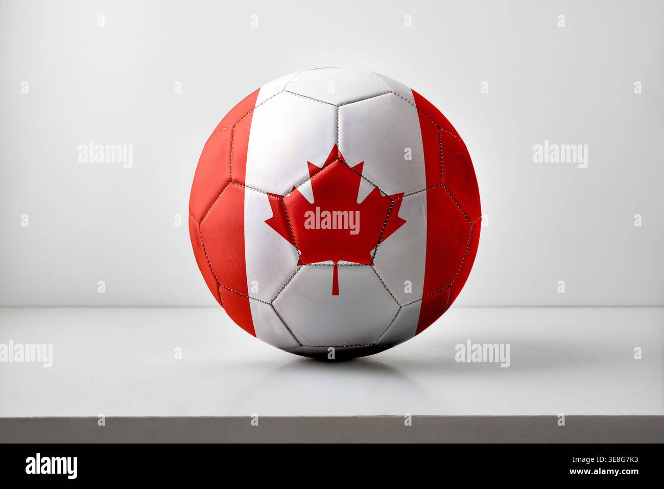 Un pallone da calcio decorato con la bandiera canadese, che mostra una foglia d'acero rosso e pannelli bianchi, collocati su uno sfondo neutro dello studio. Foto Stock
