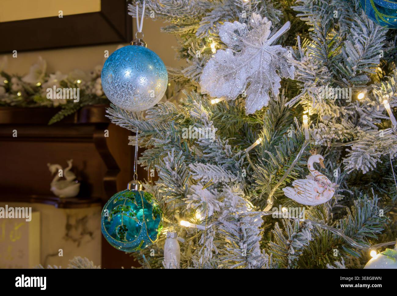 Primo piano di baule natalizie blu e bianche e decorazioni su rami di alberi smerigliati con calde luci delle fate, dettagli festivi stagionali Foto Stock