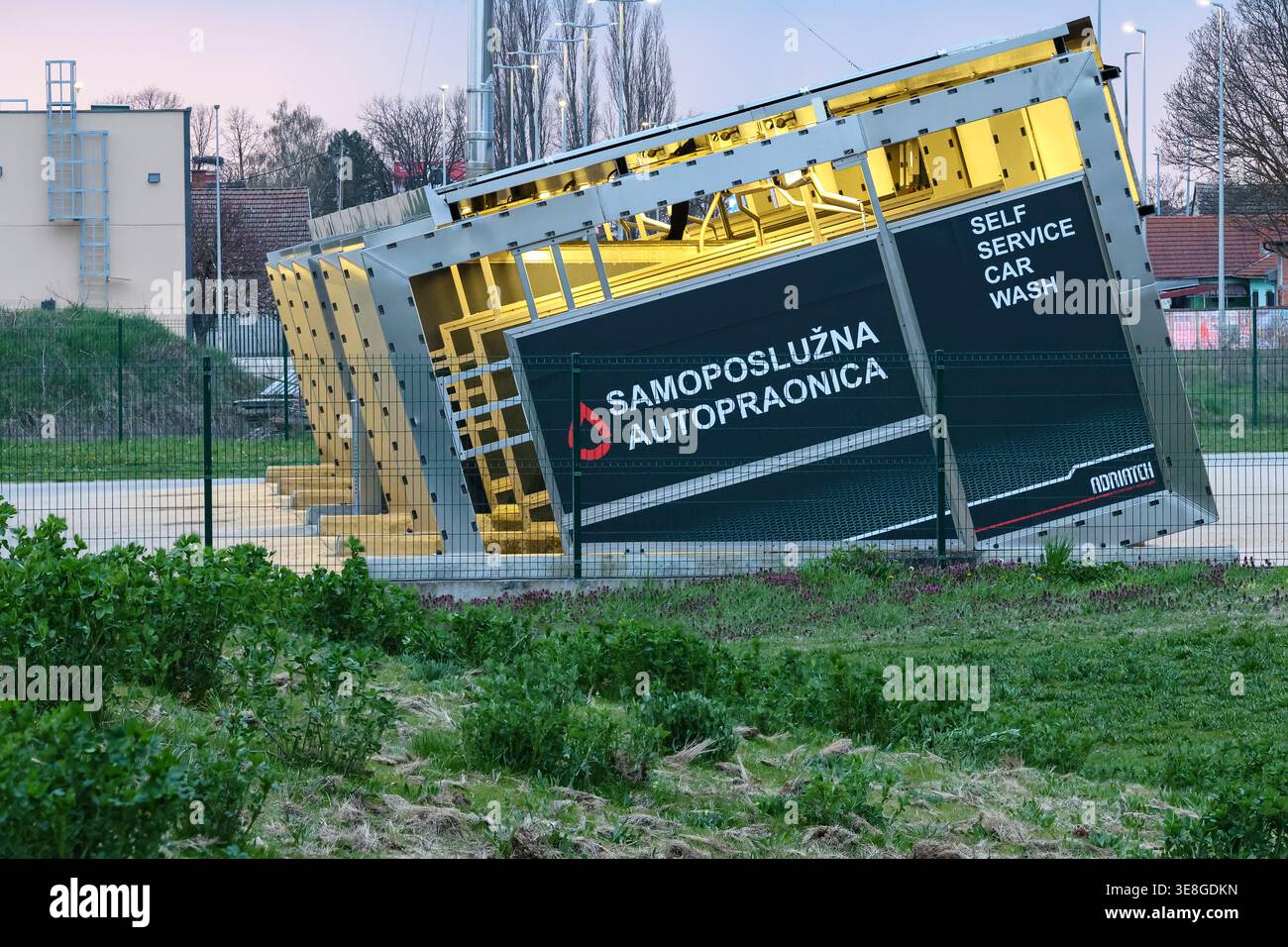 Vinkovci, Croazia - 22 marzo 2026: Aree di autolavaggio self-service inclinate presso un impianto autopraonica modulare dietro una recinzione metallica, illuminata da un punto caldo Foto Stock