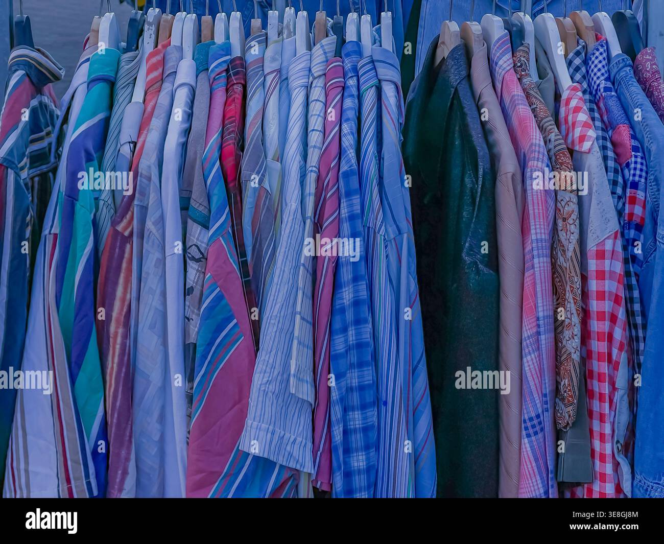 Camicie vintage colorate appese su un rack in un mercato delle pulci, una varietà di abiti preconfezionati a fantasia Foto Stock